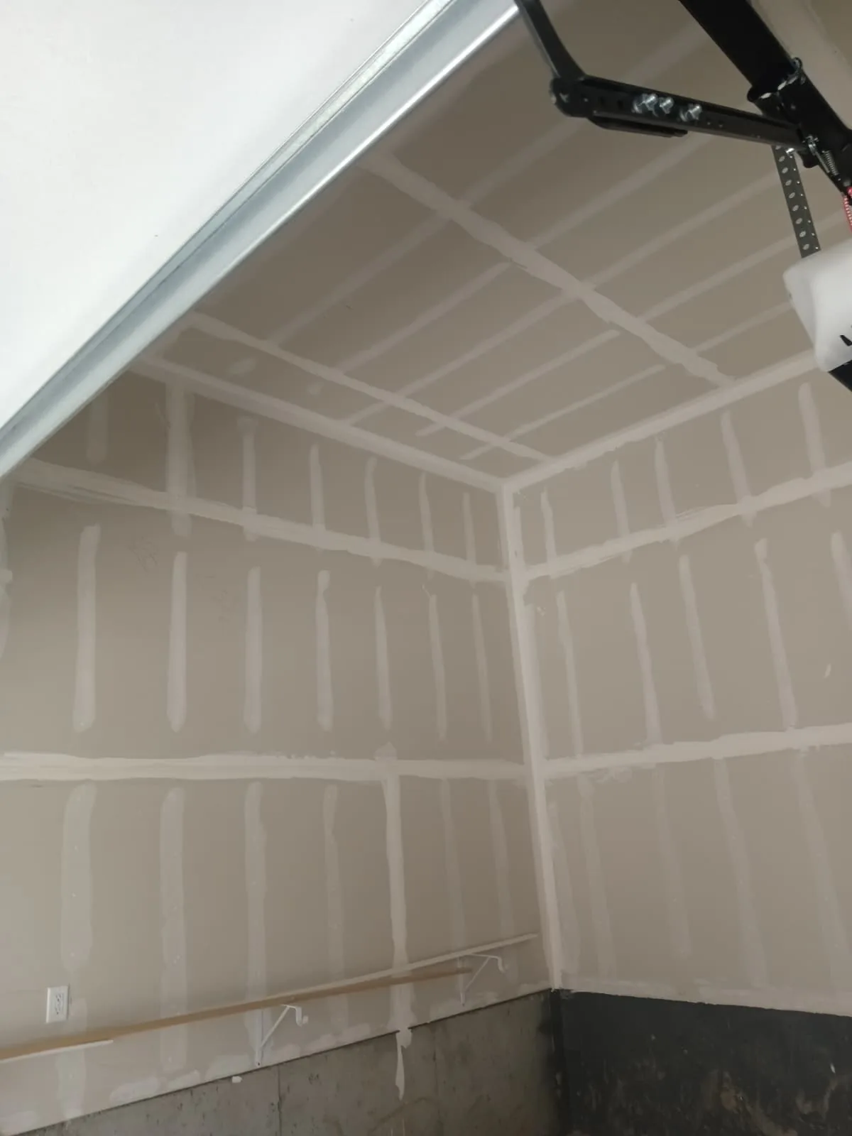 Second-coat taping in a garage — every joint feathered wide so nothing telegraphs through the finish.